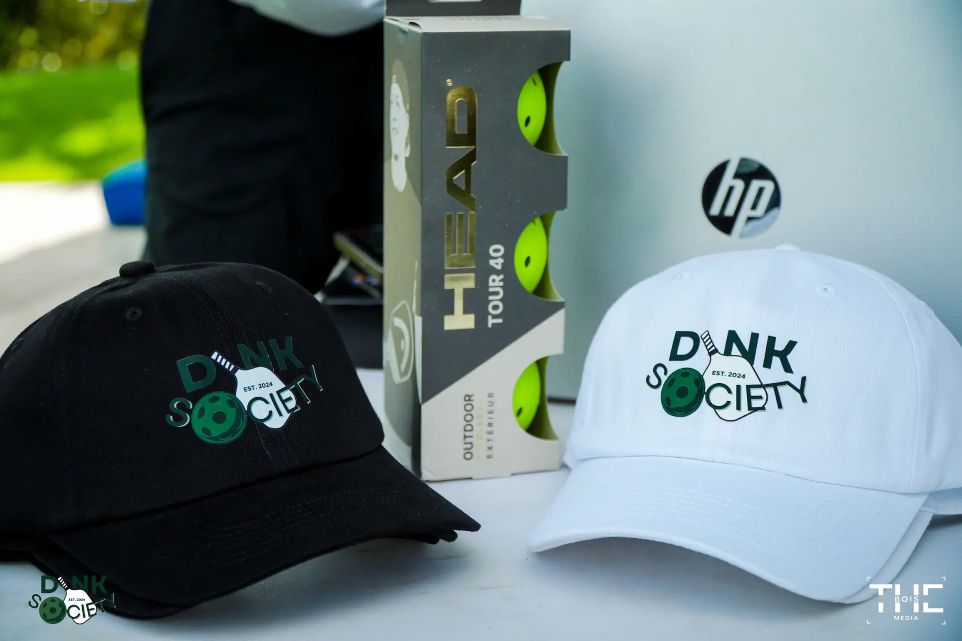 Dink Society branded hats and HEAD Tour 40 pickleball balls on a table